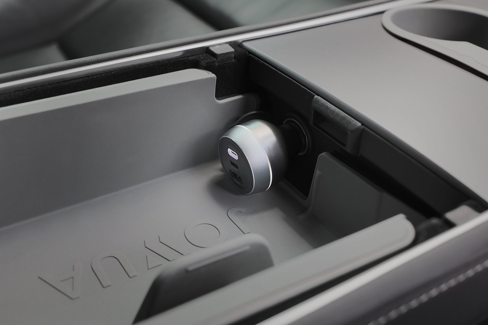 JOWUA Portable Air Compressor + Charging Solution Kit sits in the car console, plugged into a USB port amid smooth gray surfaces with 