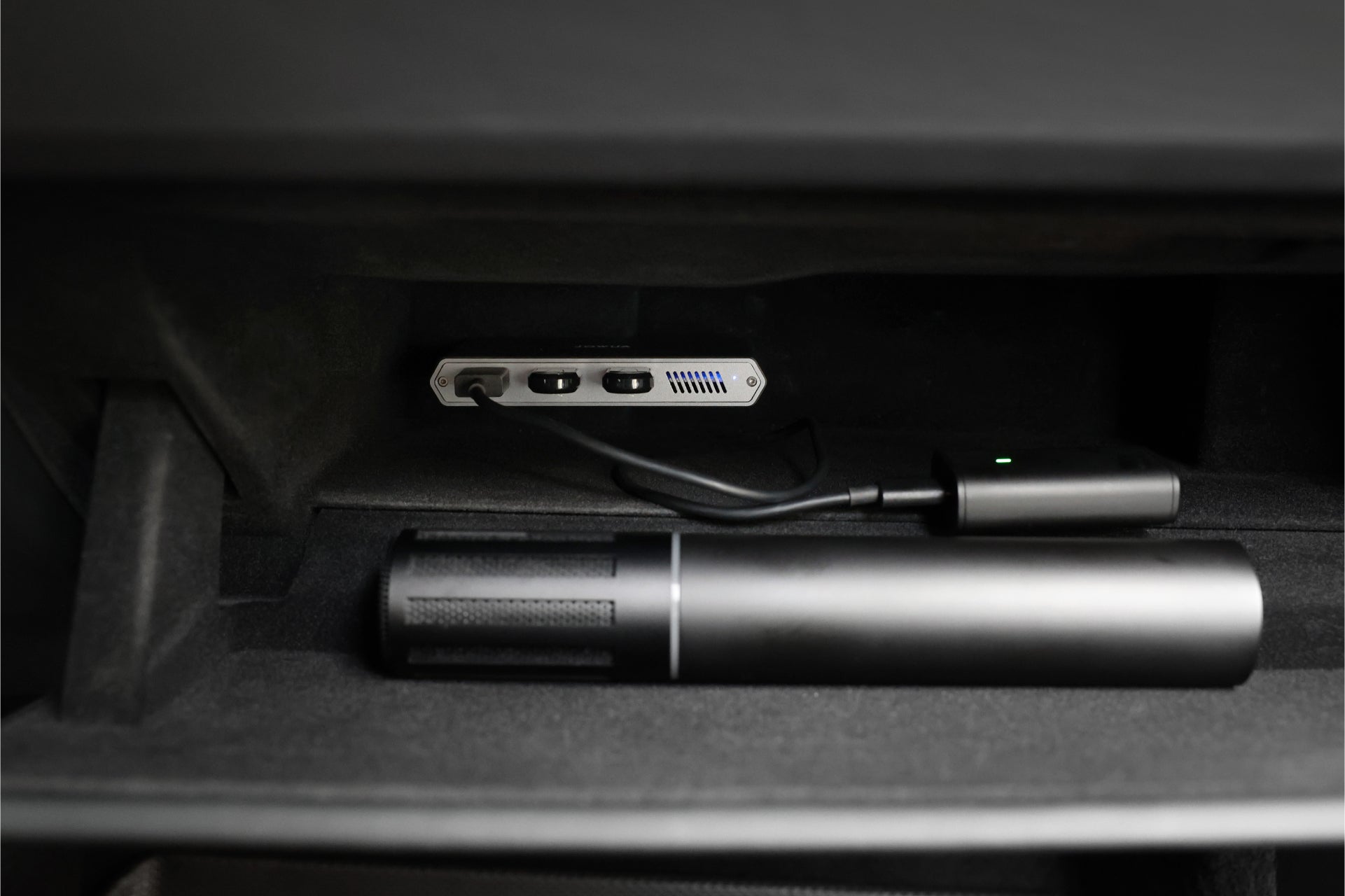 The JOWUA Tesla 1TB SSD + 3-Port HUB sits in the glove compartment near a cylindrical black object, both on a soft, dark surface—ideal for Tesla Sentry Mode storage.