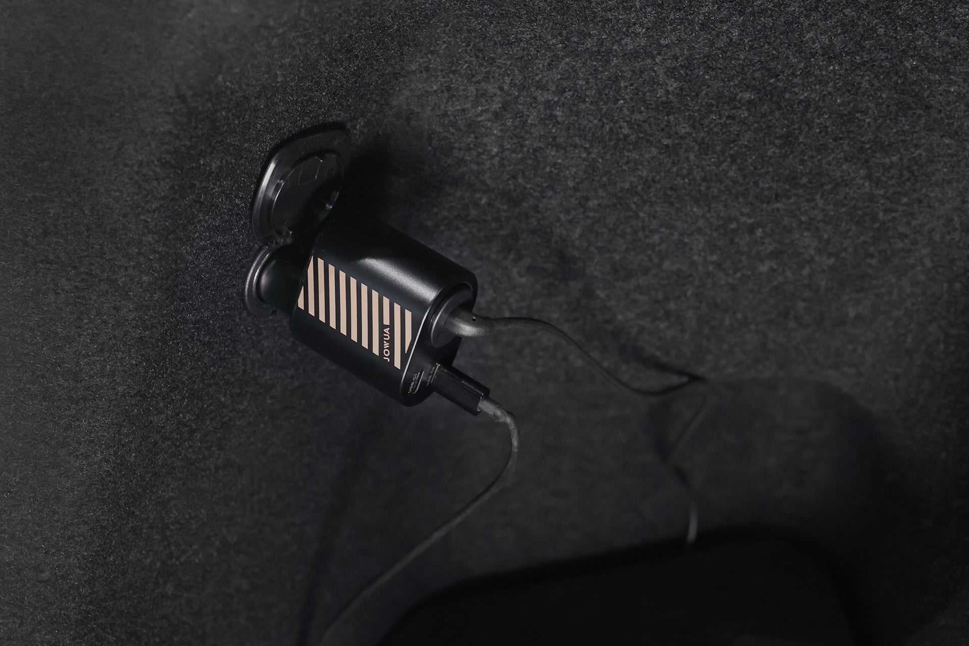 A close-up of the JOWUA 3 in 1 Type-C Car Charger plugged in, with its cable attached, set against a dark textured background.