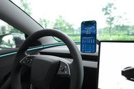A Tesla steering wheel and dashboard are shown. A JOWUA 6D Tesla Compatible Invisible Foldaway Car Mount Qi2 Wireless Charger (MagSafe) holds a smartphone beside the wheel, displaying a Los Angeles weather app. Part of the digital screen is visible on the right.