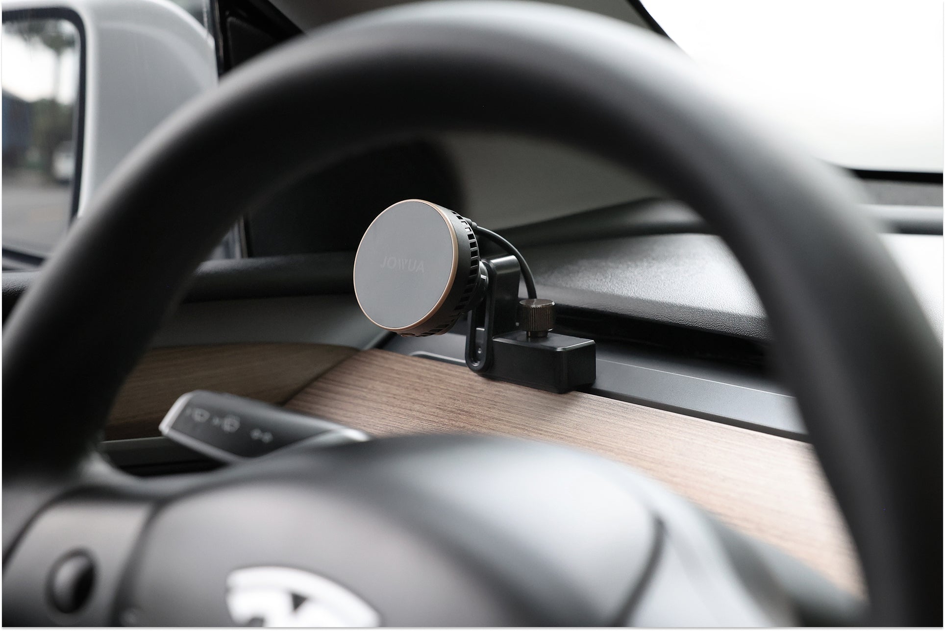 A close-up behind the wheel shows a JOWUA Active Cooling MagSafe Car Mount for Air Vents (Model 3/Y 2018-2024) attached to the dashboard, with wood trim and part of the car logo visible.