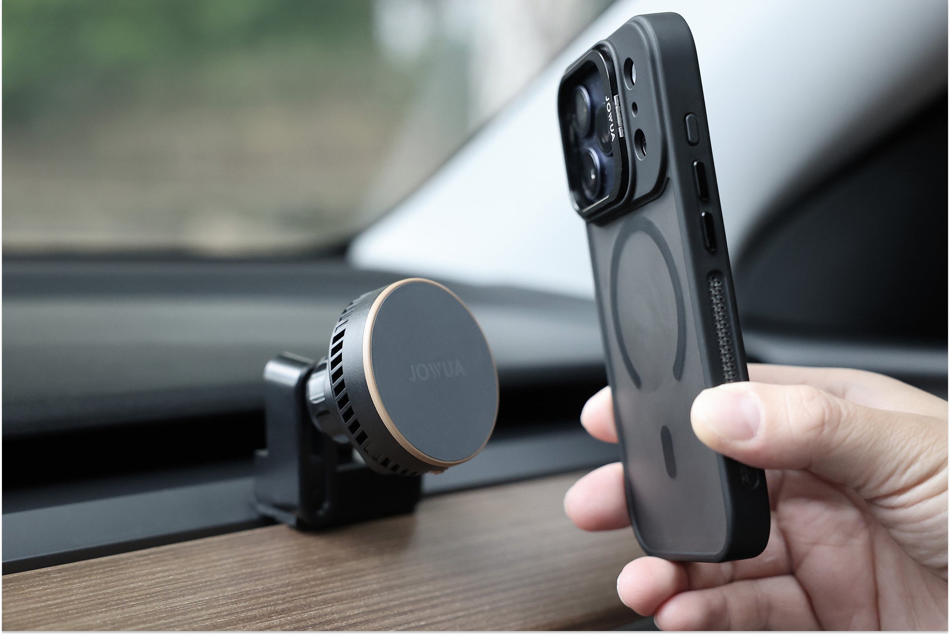 A hand holds a smartphone with a visible magnetic ring near the JOWUA Active Cooling MagSafe Car Mount for Air Vents, designed for Model 3/Y (2018-2024), securely attaching to a wood-trimmed dashboard and showcasing seamless compatibility.
