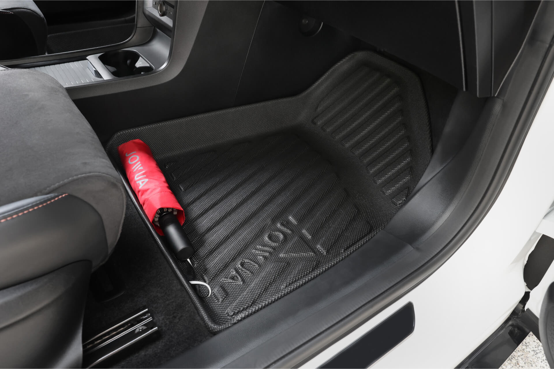A close-up view of the front passenger footwell shows a black JOWUA All Weather Floor Liner (MG MG4) with a red umbrella placed on it near the seat.