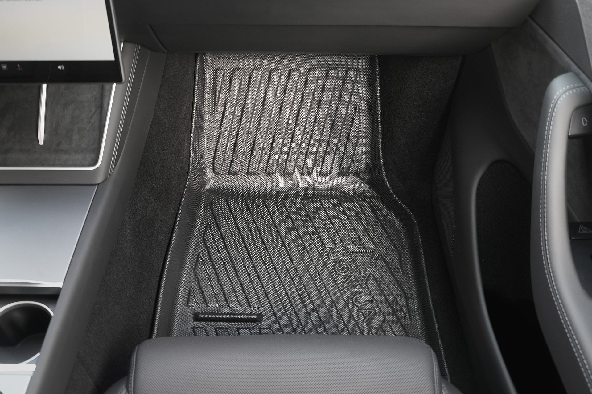 A black textured JOWUA Model Y L (2026+) All Weather Floor Liner (Left Hand Drive Version) is placed in the front passenger footwell of a modern car, surrounded by sleek black and silver panels.