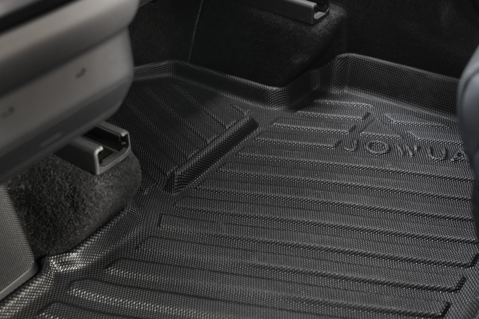 Close-up of the JOWUA Model Y L (2026+) All Weather Floor Liner (Left Hand Drive), shown in black with a textured surface, raised edges, and grooves to trap dirt and moisture, fully covering the carpeted area under the dashboard and seat.