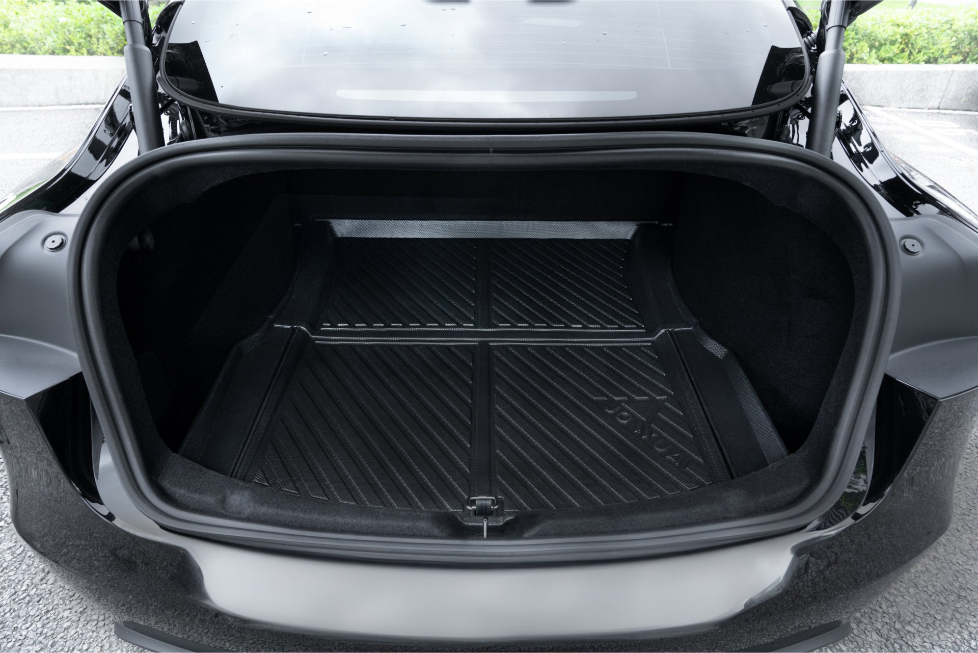 The open trunk of a black Tesla Model 3 features the Model 3 All Weather Trunk Combo by JOWUA, showcasing a clean, empty interior lined with a black textured rubber mat made from waterproof TPE material. With its grooves and the "Tesla" embossment near the back, the well-lit space underscores its spacious cargo area.