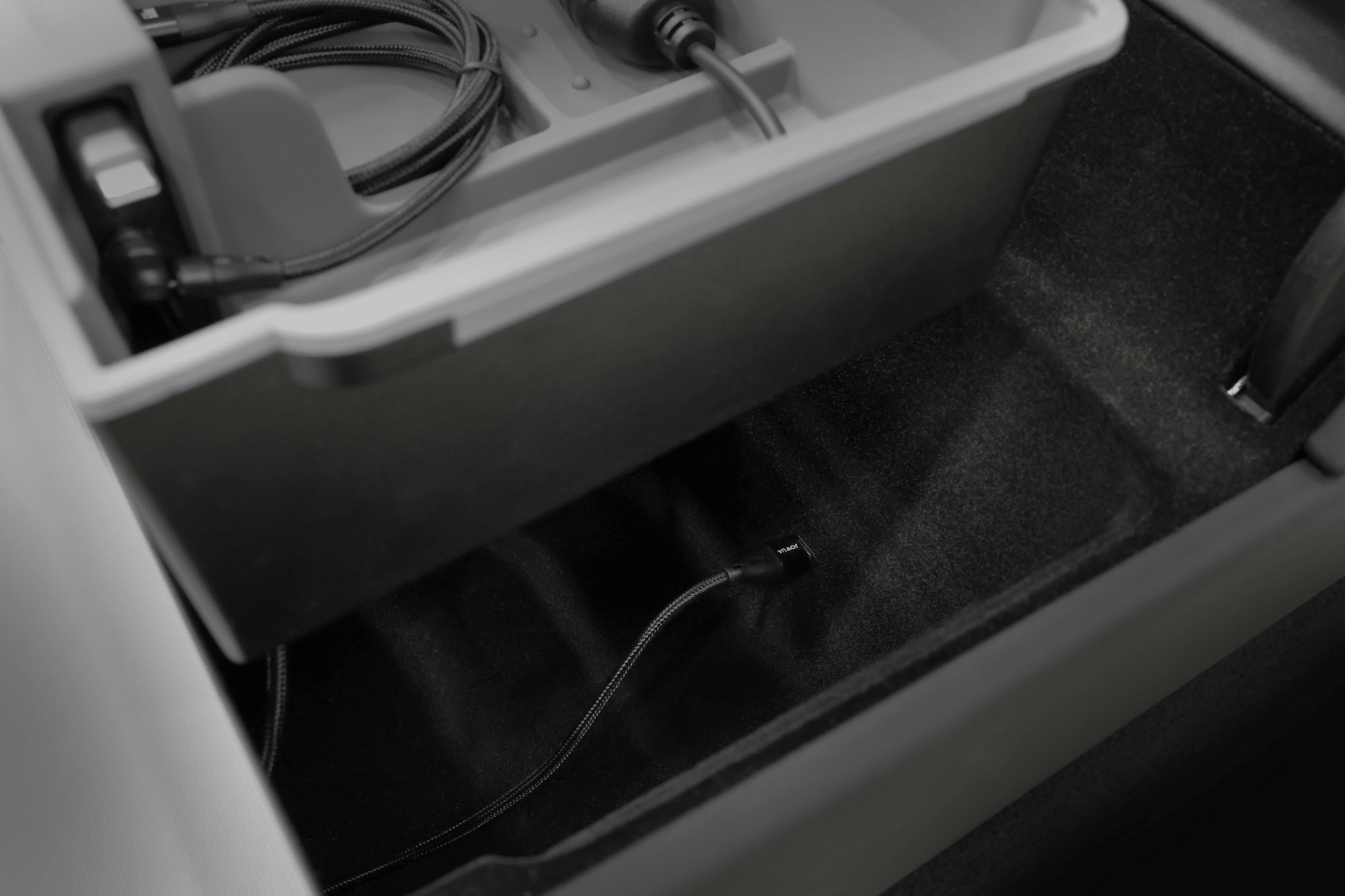 A close-up view of a JOWUA Center Console Organizer Set with Power HUB (Tesla Model 3 Standard 2026+), showing a plastic tray for charging cables and a USB cable extending into the spacious compartment below.