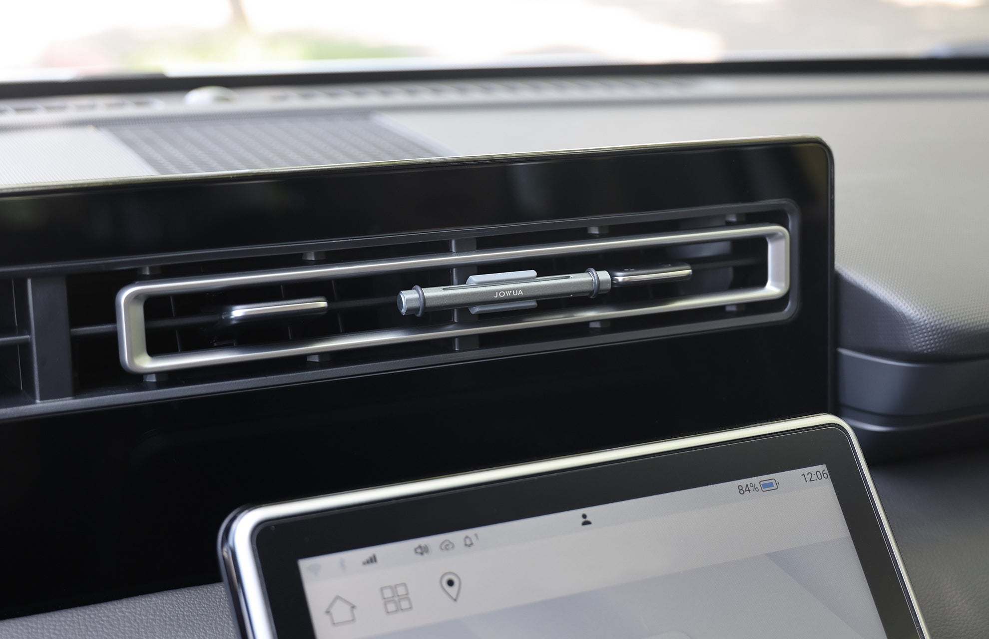 A close-up of a car's dashboard air vent with a pen above the touchscreen features the JOWUA Tesla Air Freshener for Model S/3/X/Y, offering natural scents and a silicone base for secure placement.