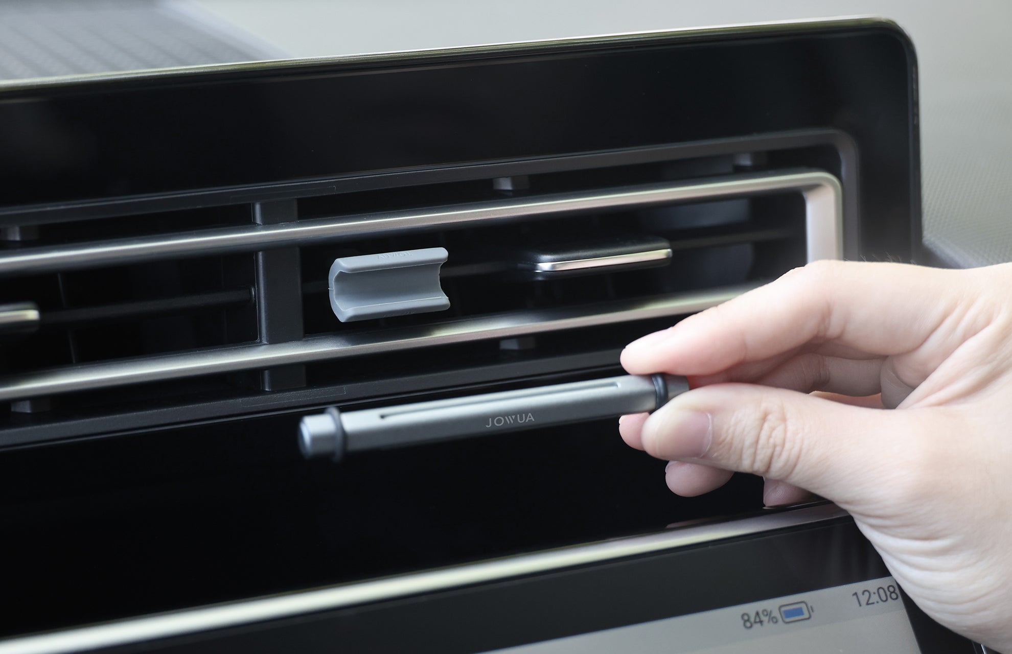 A hand adjusts a JOWUA Tesla Air Freshener for Model S/3/X/Y with a silicone stabilizing base near a car's air vent, while the dashboard display is visible in the bottom right corner.
