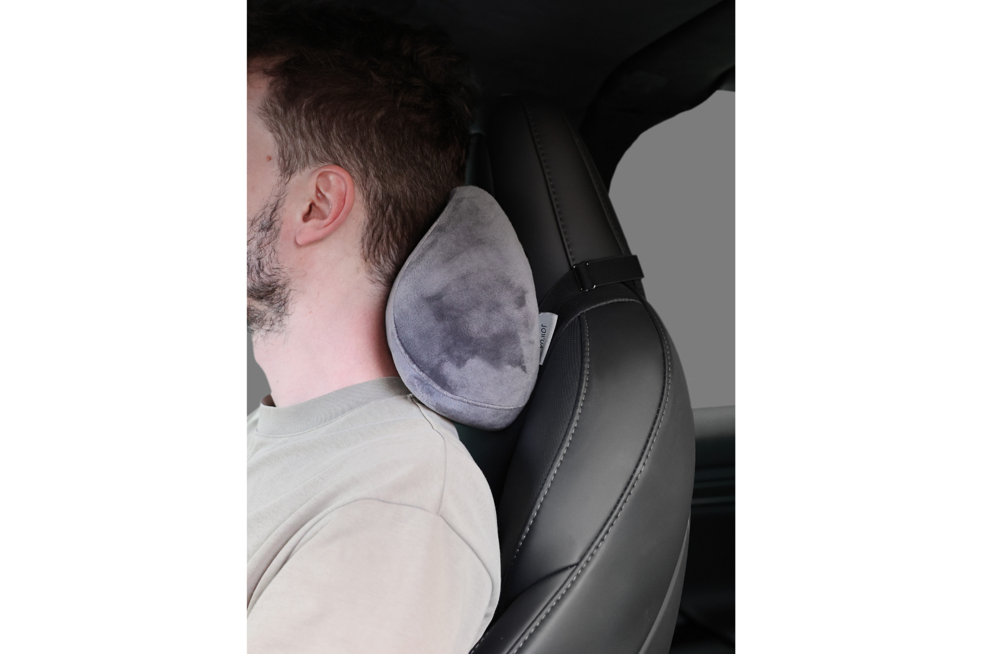 A man uses the JOWUA Car Neck Pillow, a soft gray memory foam cushion attached to his car’s headrest, for enhanced comfort and ergonomic support while driving.