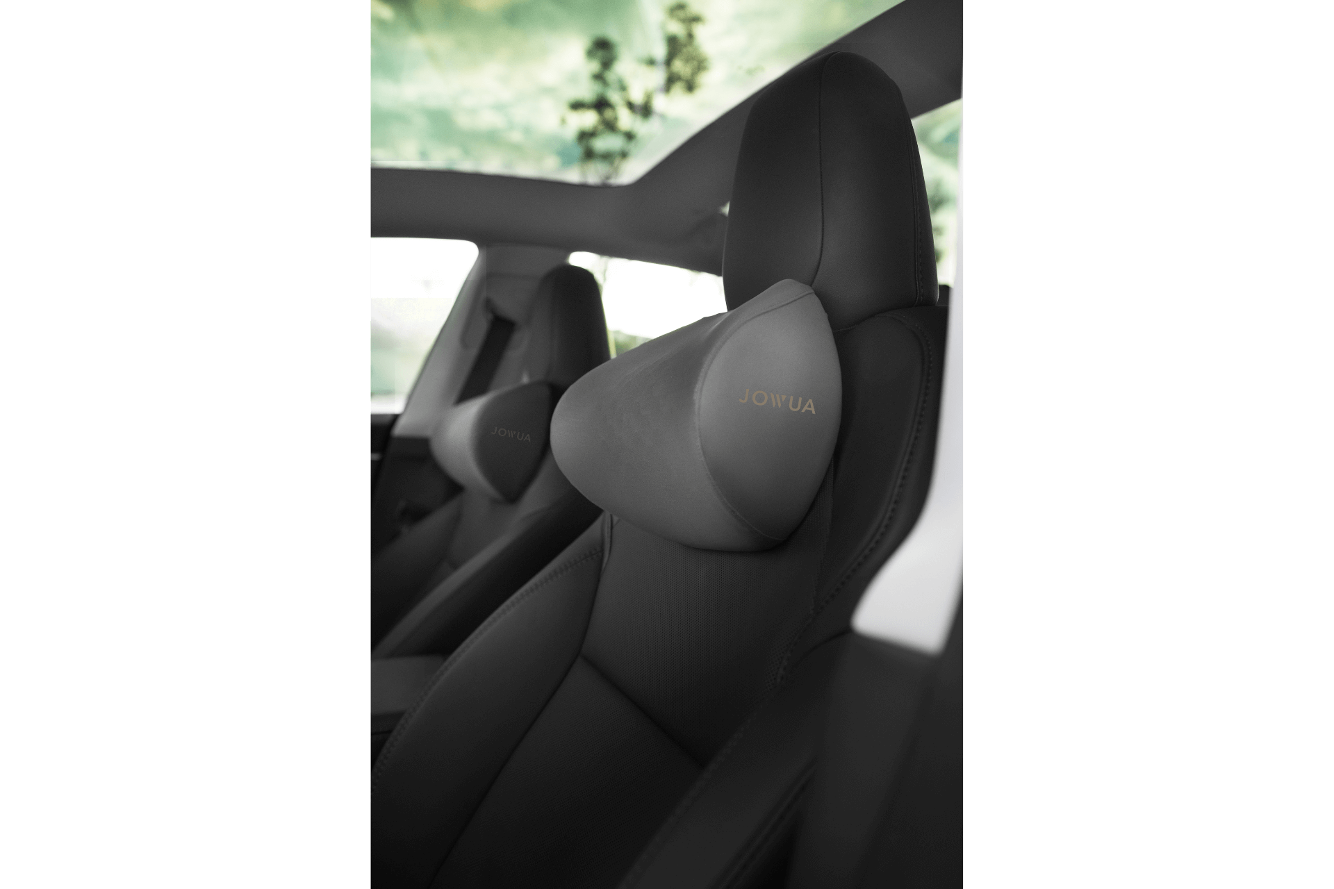 Close-up of a car front seat with a gray JOWUA Car Neck Pillow attached to the headrest; a large sunroof shows blurred trees and sky above.