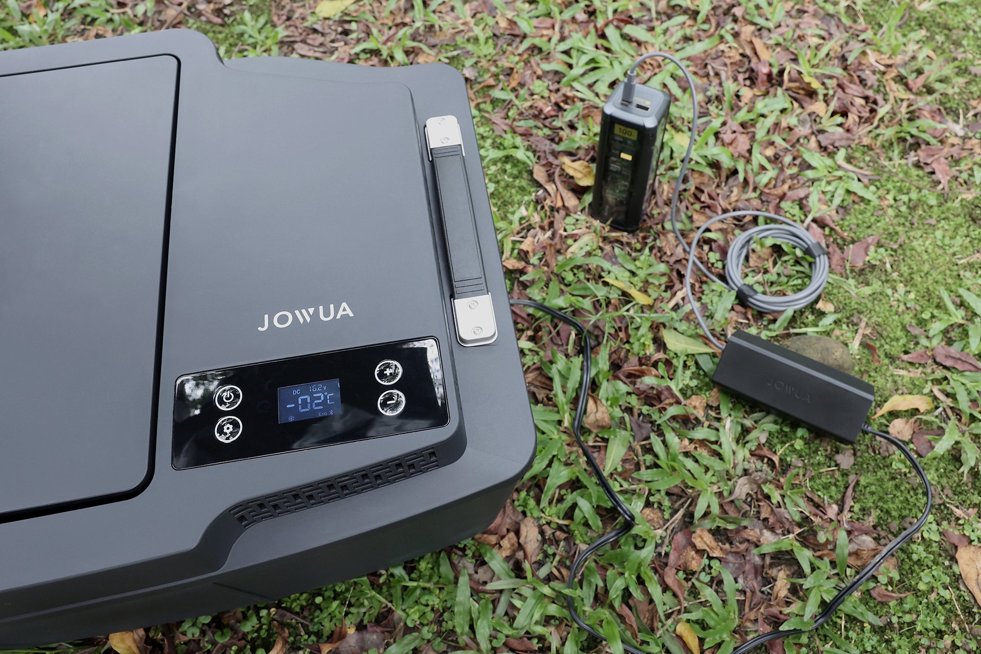 The JOWUA Car Refrigerator for Tesla Model Y, featuring a digital display showing -2°C, sits on grass powered by a connected power bank and cables, and offers intelligent dual-mode cooling for optimal performance.