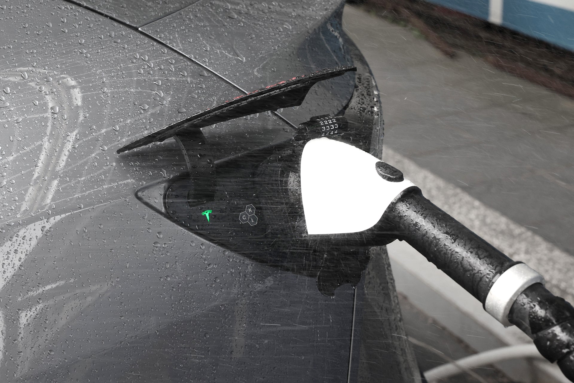A JOWUA CCS1 to CCS2 DC & AC Combined Adapter connects an electric vehicle for fast charging at a station in the rain, with water droplets visible on its surface.