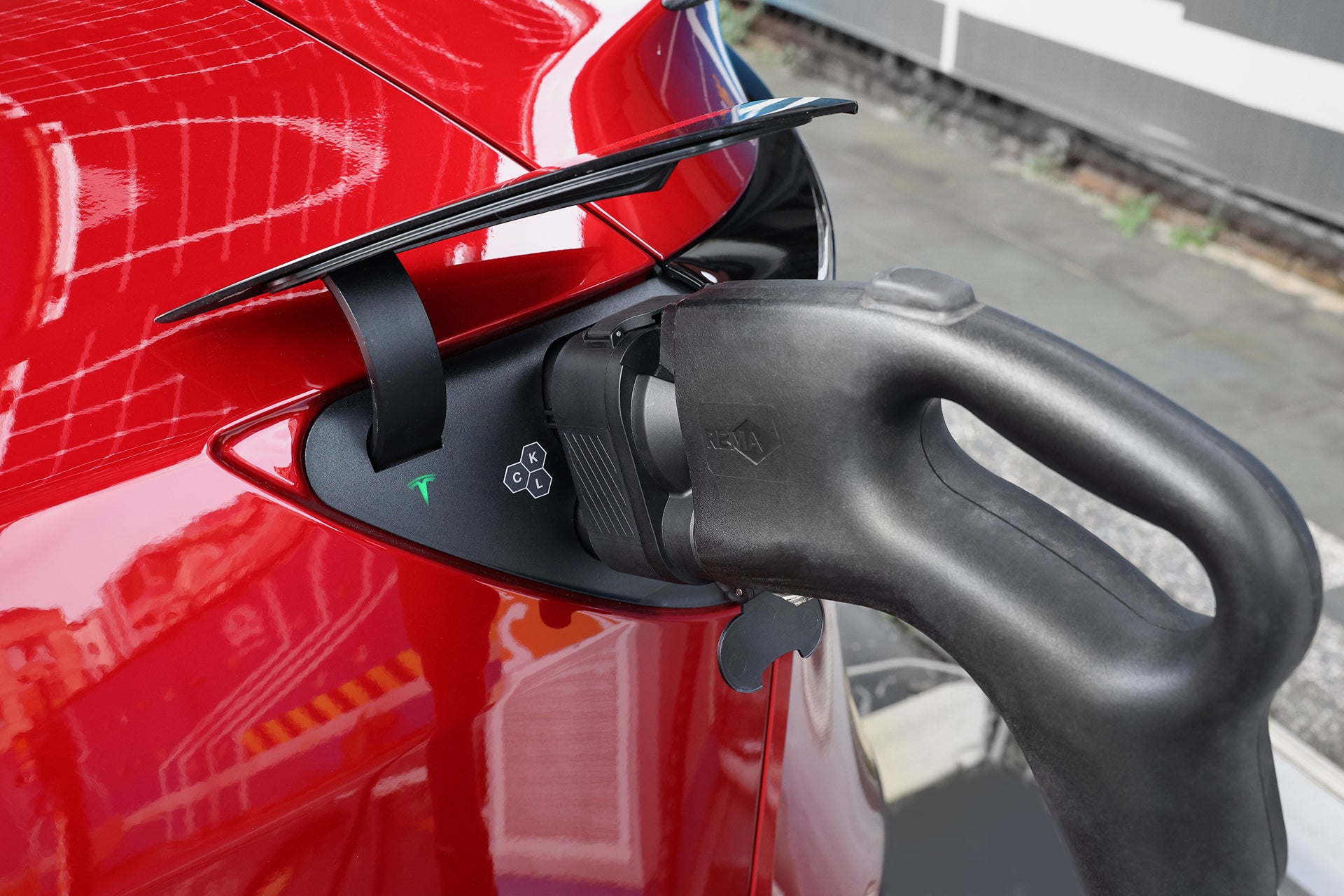 A close-up of the JOWUA CCS1 to CCS2 DC & AC Combined Adapter plugged into a red electric car, with building reflections on its surface, showcasing reliable EV charging compatibility.