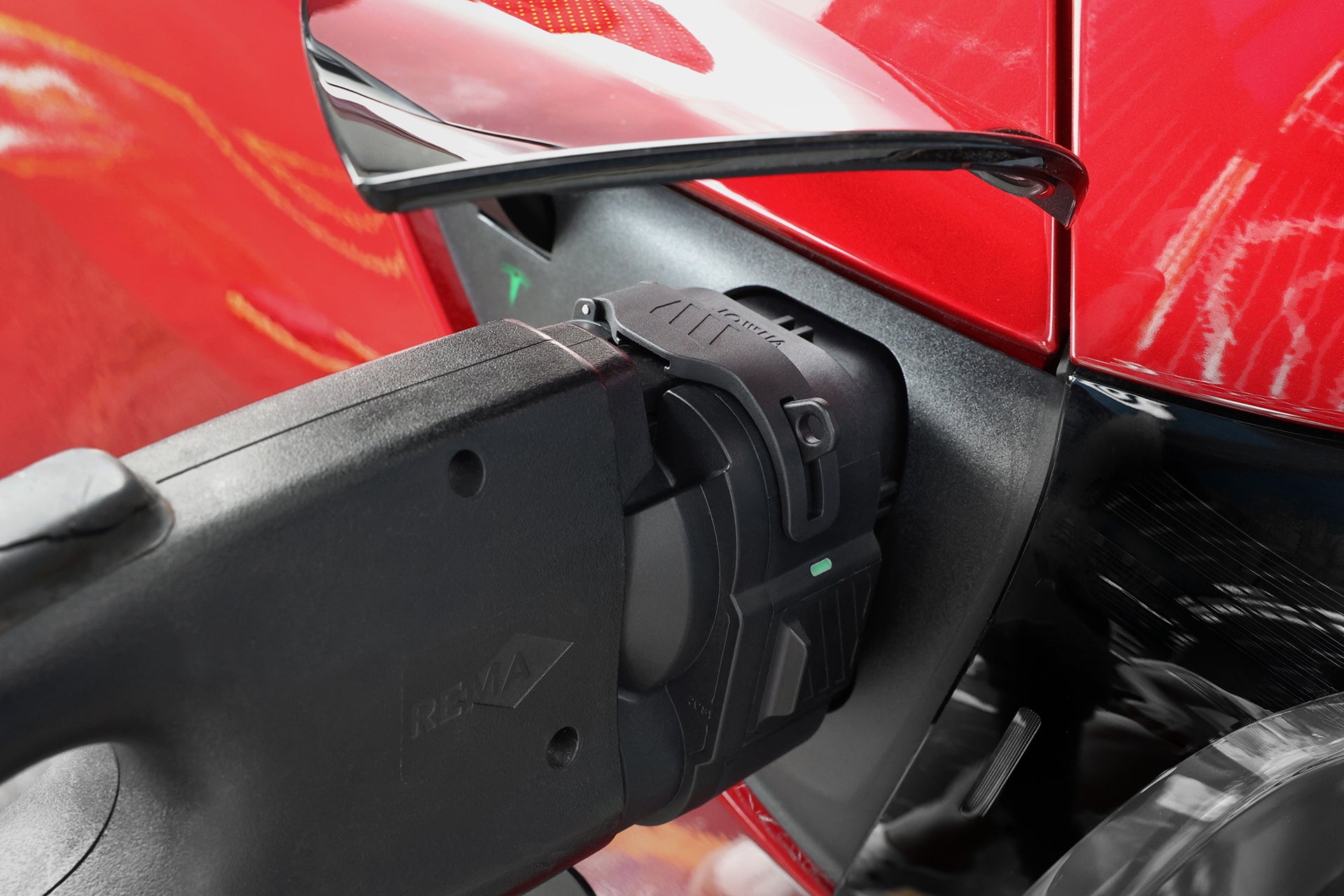 Close-up of a red car using the JOWUA CCS1 to CCS2 DC & AC Combined Adapter in its charging port, showcasing EV charging compatibility and part of the side mirror.