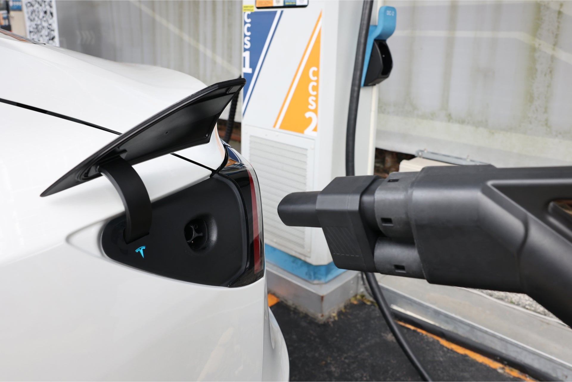 A white electric car is being charged at a station using the JOWUA CCS2 to NACS DC Charging Adapter. The connector is securely plugged into the car