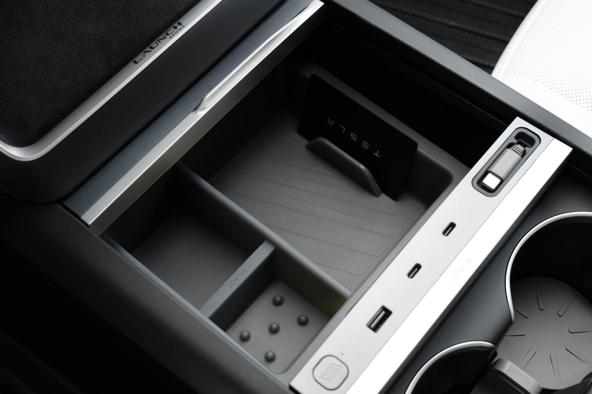 Open the center console of a Tesla Model Y Juniper (2025+) featuring JOWUA's LED Center Console Combo with silicone organizer, storage compartments, USB ports, cup holders, and a black partition branded with "Tesla.