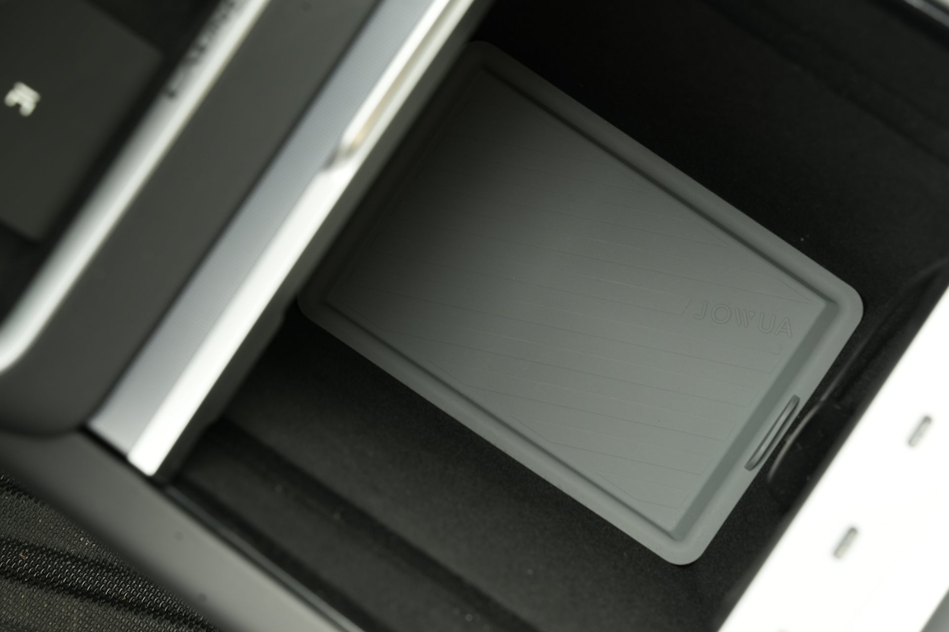 A close-up of a gray rectangular JOWUA Center Console Set (Tesla Model Y Juniper 2025+) placed in a car's storage compartment, partially surrounded by black and white surfaces—ideal for Tesla Model Y Juniper interiors.