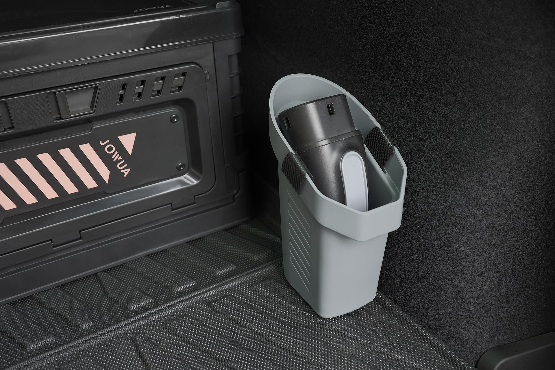 A small black vacuum cleaner sits in a gray Tesla trunk bin next to a JOWUA Door Side Storage Box (Set of 2) with a diagonal pink striped label.