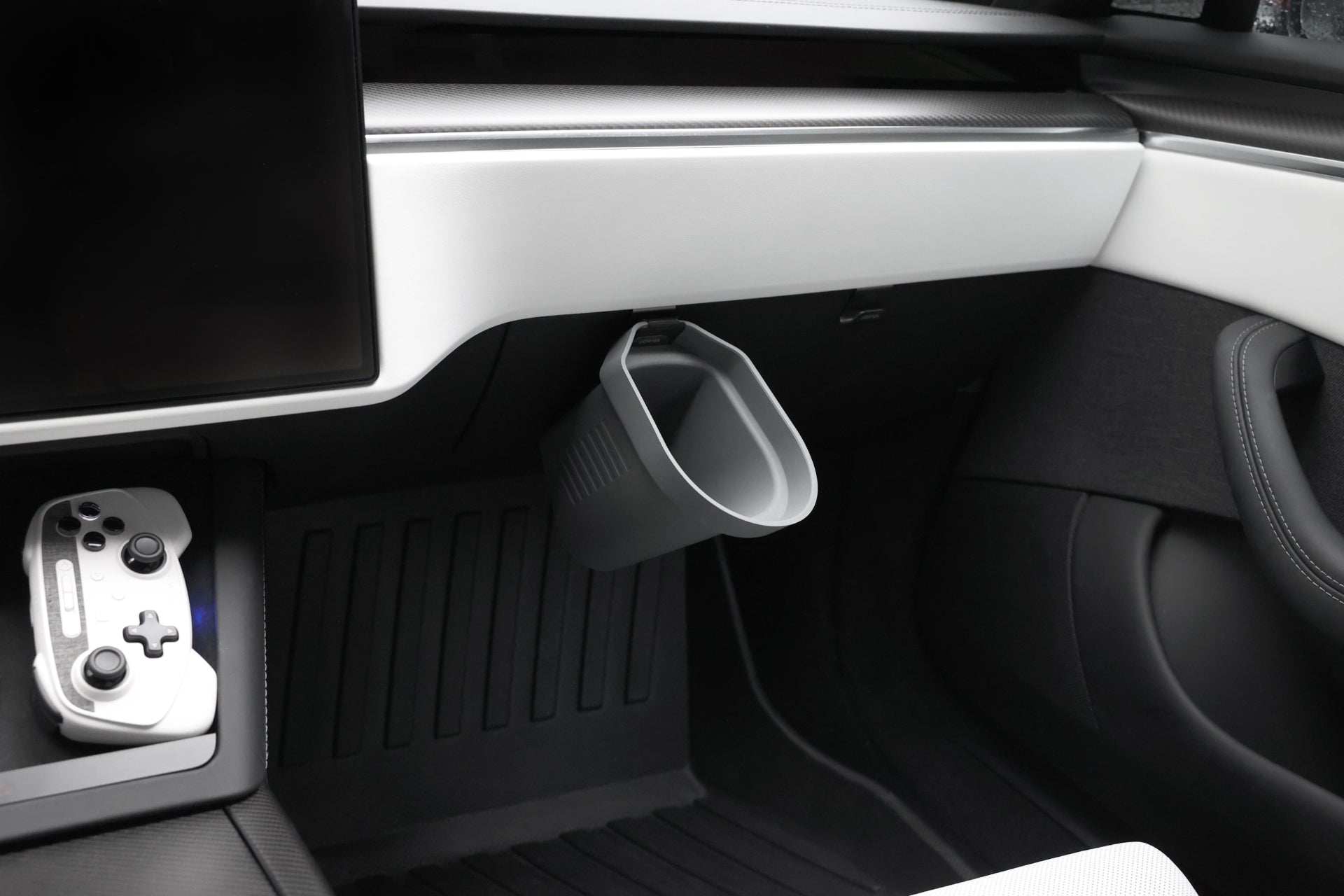 The car's interior showcases a modern, minimalist design similar to Tesla Models. A game controller is positioned on the center console, and a sleek gray silicone waste bin is attached to the passenger side dashboard. To the left, there is a partial view of a large screen. Additionally, a set of JOWUA Door Side Storage Boxes adds to the car's organized feel.