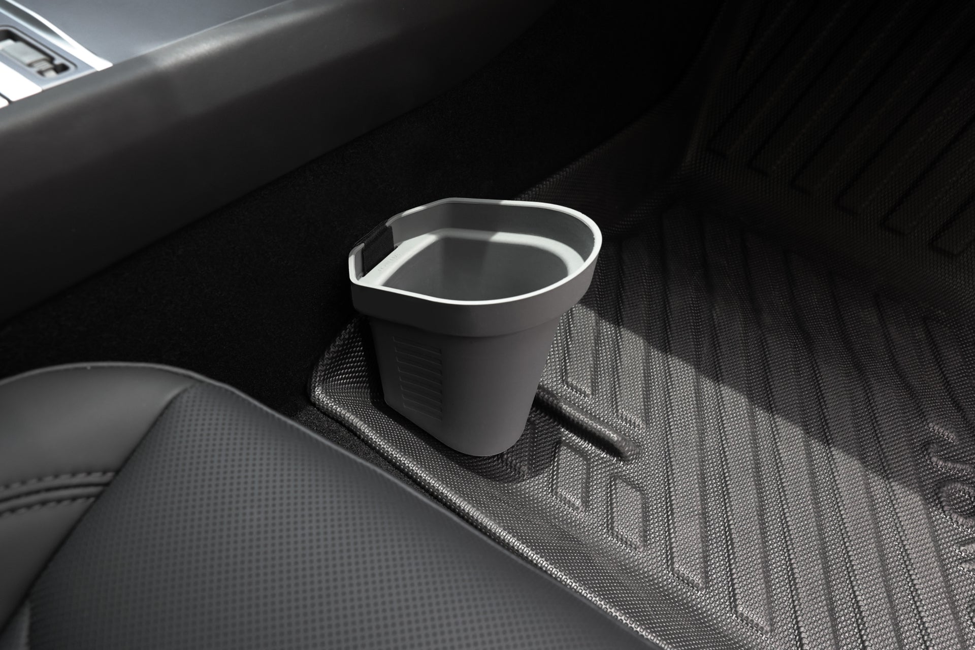 A small, gray JOWUA Door Side Storage Box from a set of two is made of silicone material and placed on the floor of a Tesla Model S with black textured mats. It is positioned next to the passenger seat, near the door, fitting snugly against the floor contours.