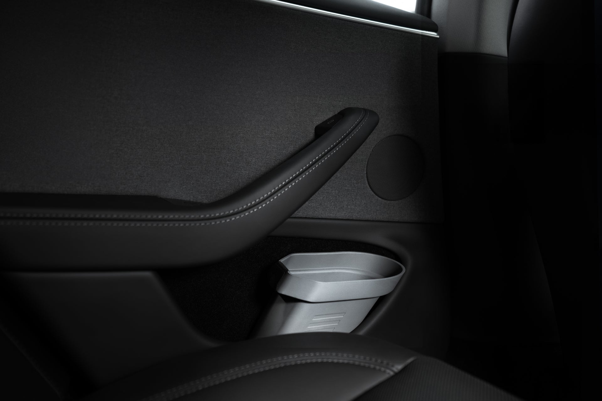 The interior view of a JOWUA door side storage box for Tesla Model showcases a sleek, dark panel crafted with silicone material. It features an armrest, cup holder, and discreet storage bin. The minimalist design is accentuated by smooth surfaces and a small speaker seamlessly integrated into the door.