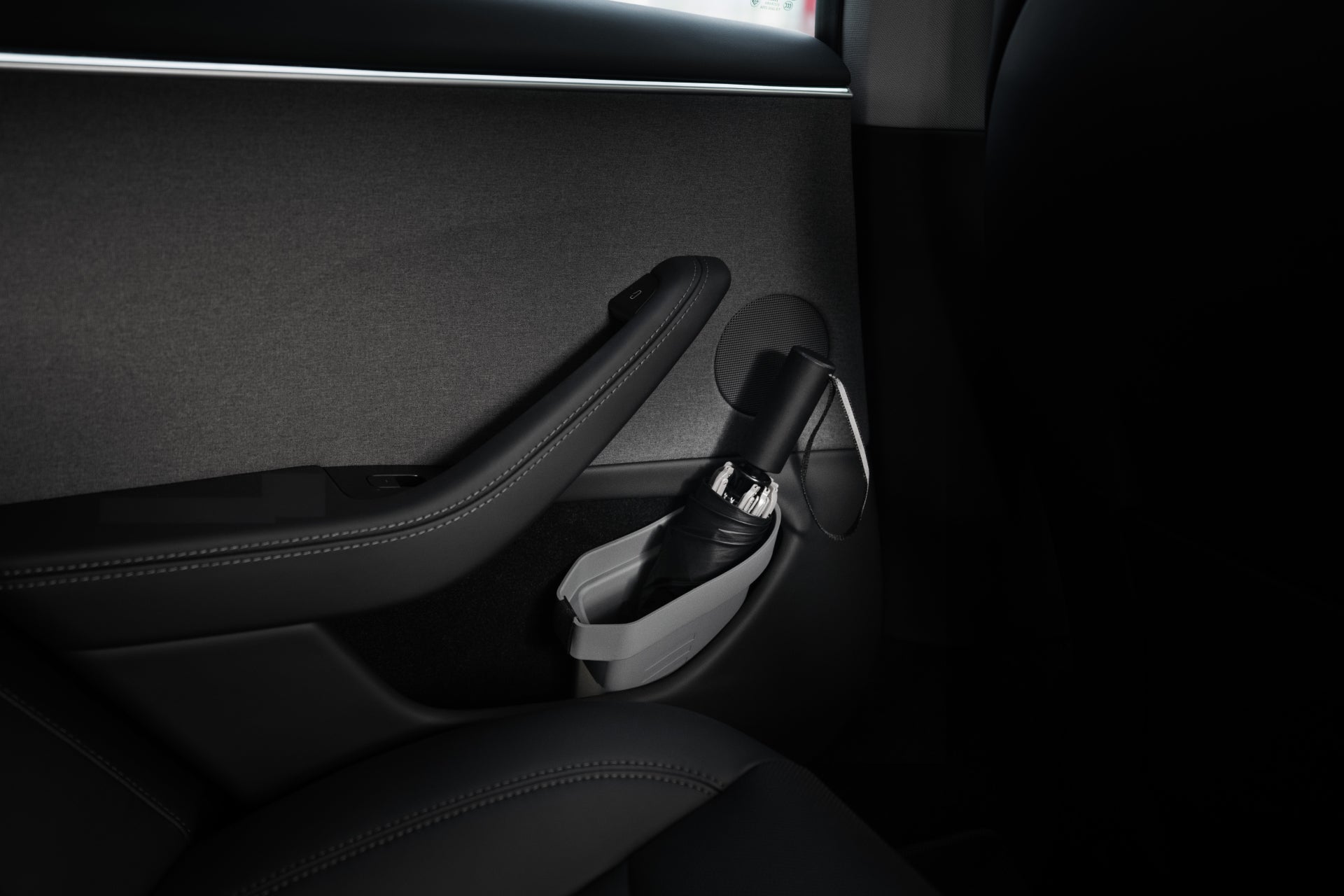 Interior view featuring a Tesla Model's door equipped with a JOWUA Door Side Storage Box that showcases a dark gray armrest and integrated storage bin. A cup holder cradles a small black water bottle, surrounded by subtle stitching details on the upholstery. The sleek background enhances the sophisticated design.