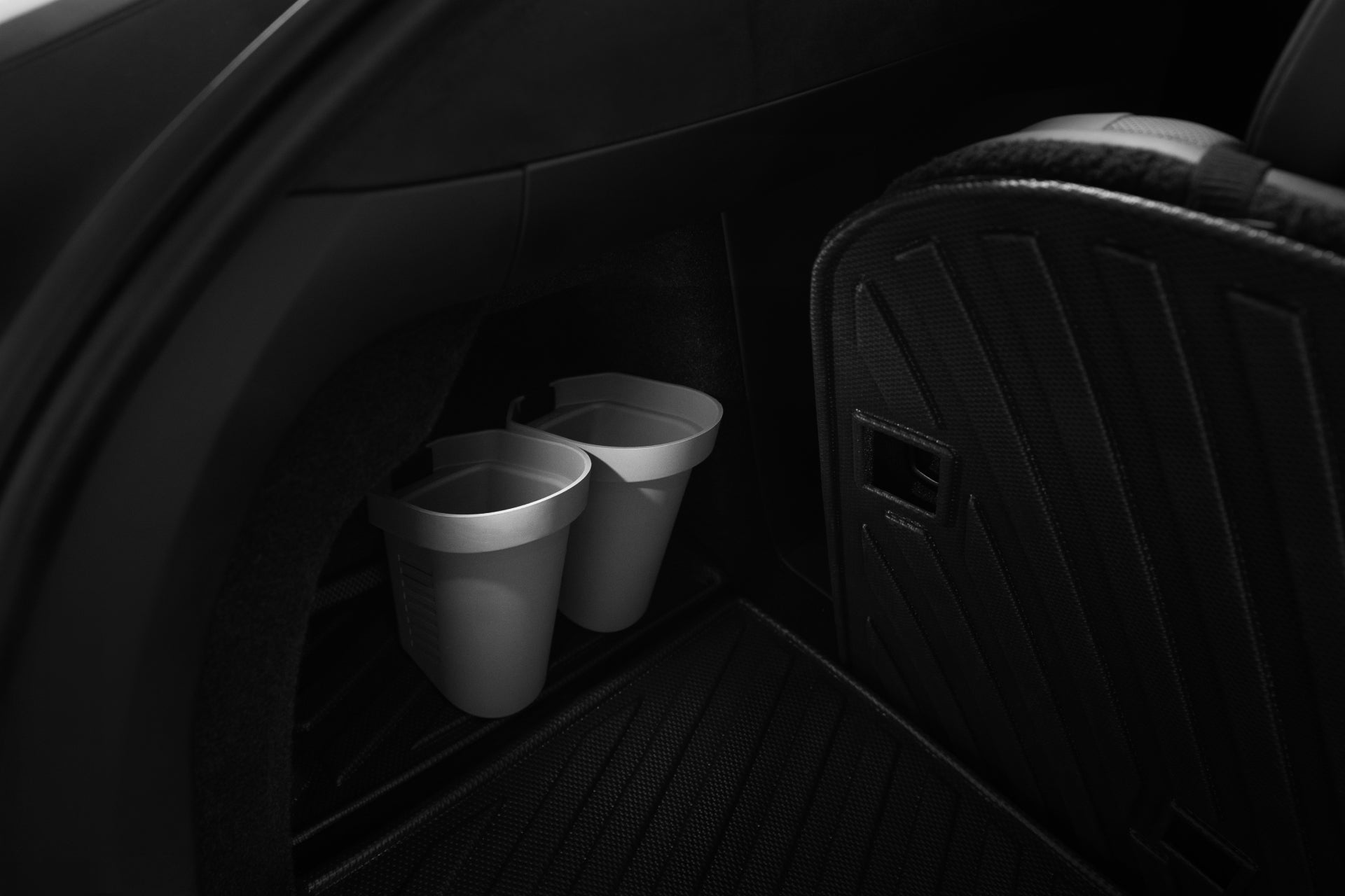 A set of JOWUA Door Side Storage Boxes is elegantly attached to the side of a car seat. They seem perfectly designed for holding beverages, and the seat is covered in textured black silicone material. The dim lighting highlights the curves and details beautifully.