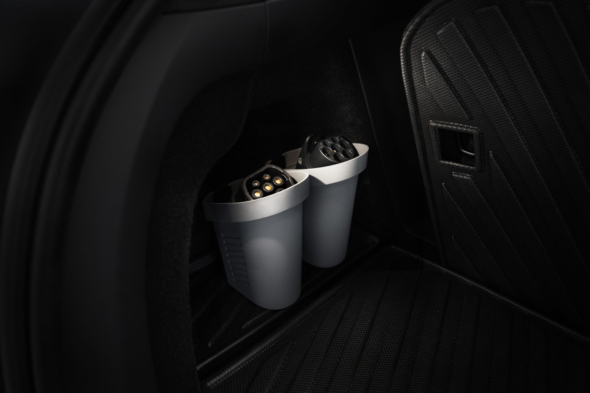 A close-up of a Tesla Model's interior features the JOWUA Door Side Storage Box set, with two bins neatly storing EV charging cables. These durable silicone storage boxes rest in a compartment with a textured black surface, emphasizing the vehicle's organized and efficient design.