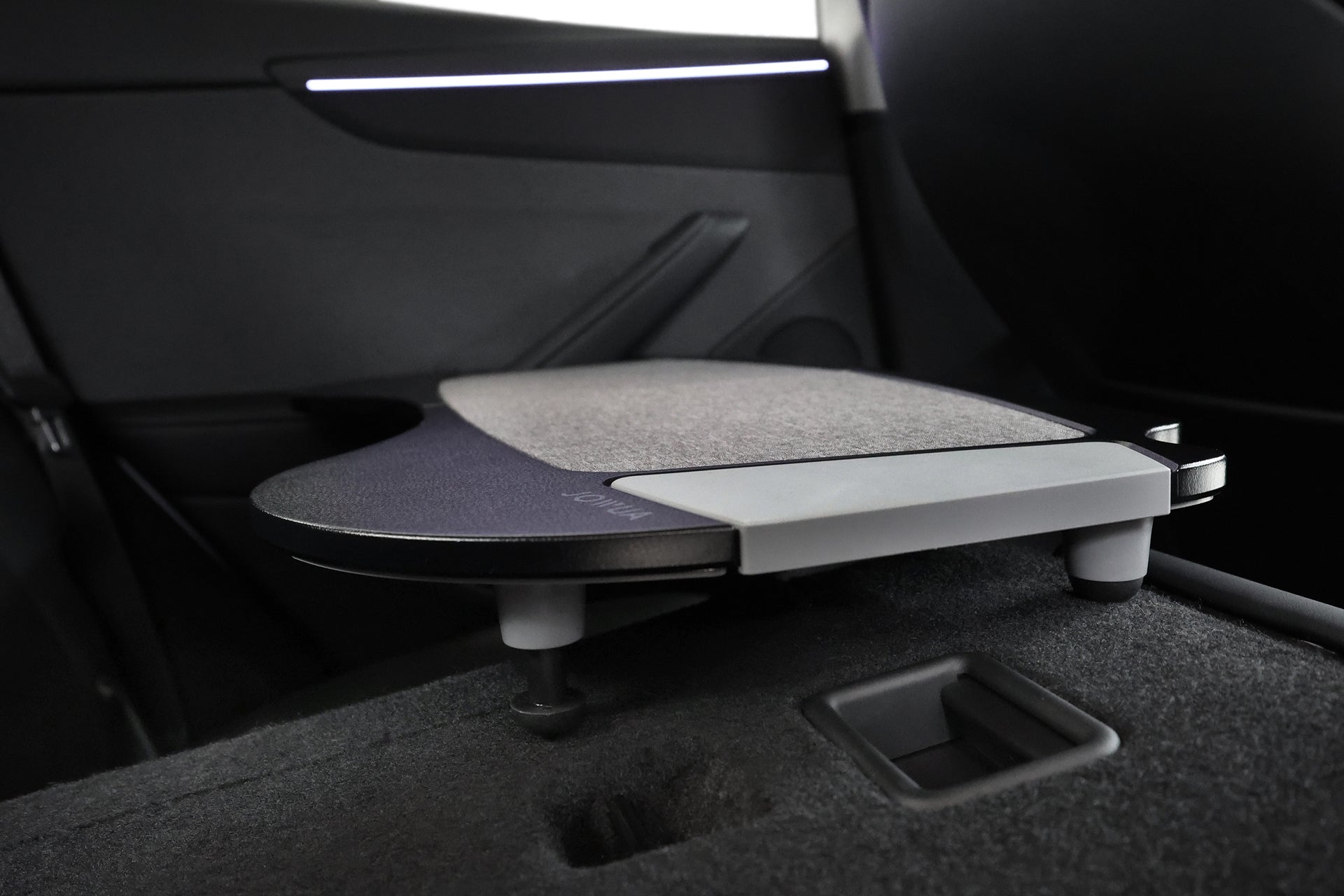 A close-up of the JOWUA Foldable Car Tray for Tesla extended in the rear seat, showing its textured surface and modern design, with the car’s interior door and seat in view—an innovative accessory for Tesla vehicles.