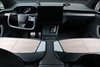 The interior of a Tesla showcases a minimalist design with premium materials, including a steering wheel, large central touchscreen, and wood-accented dashboard. In this modern and sleek setting, the JOWUA Foldable Car Tray perfectly complements the gear selector and two pedals.