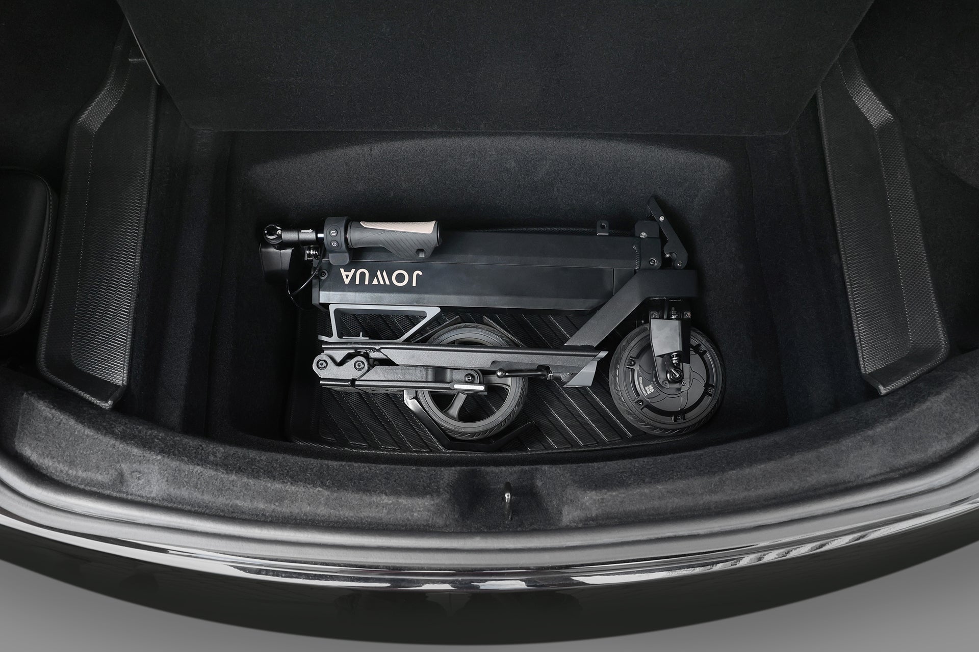 A folded black Folding Electric Scooter｜Performance by JOWUA sits neatly in a car trunk, ready to provide luxury ride comfort wherever your journey leads.