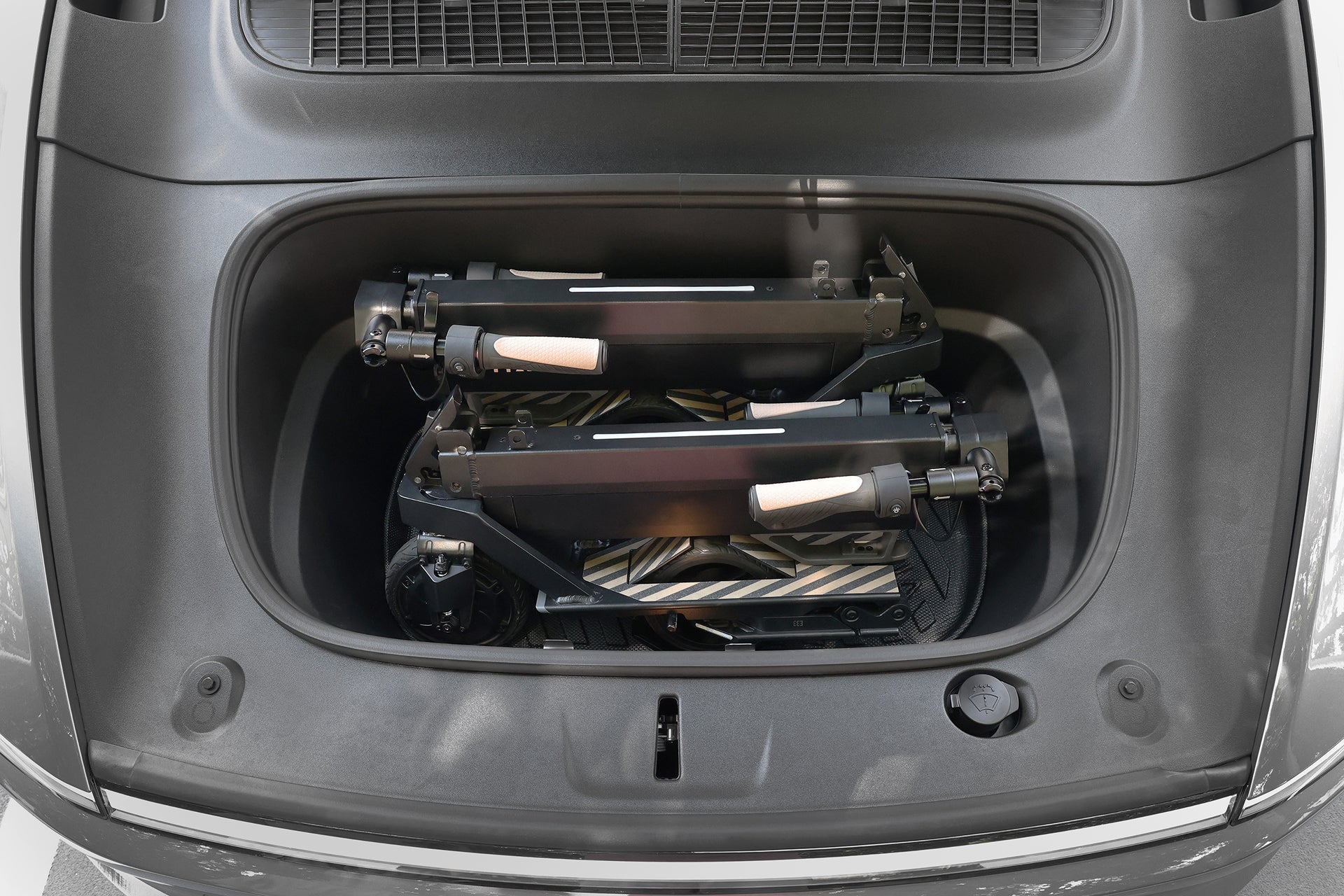 Two JOWUA Folding Electric Scooter｜Performance models with long-range batteries and light-colored handles are stored neatly inside a car's clean, spacious front trunk (frunk) compartment.