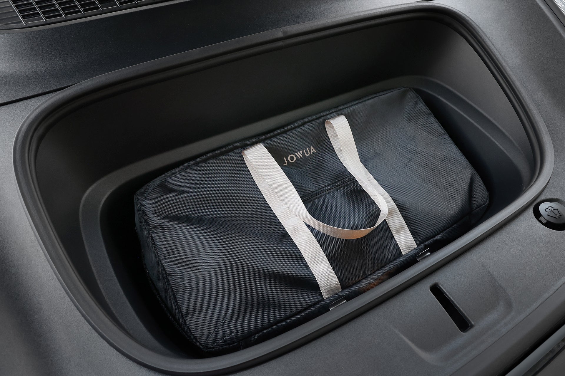 A black bag with white handles labeled "JOWUA" sits in the vehicle's frunk, designed to carry the Folding Electric Scooter｜Performance for luxury ride comfort.
