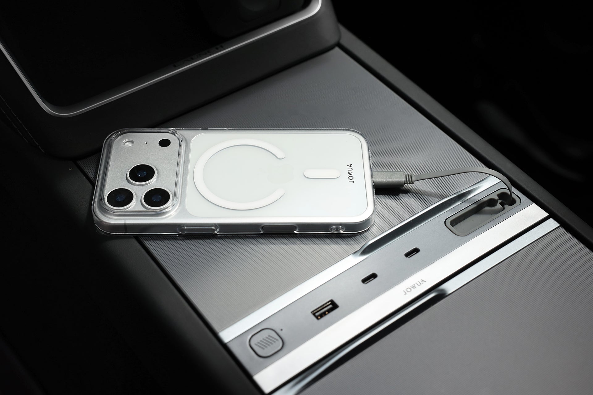 A JOWUA iPhone Case for Tesla Car Mount with MagSafe + Phone Tether Tab Set (iPhone 17 Series) securely connects the phone by cable to the car’s USB charging port in a sleek metallic center console.