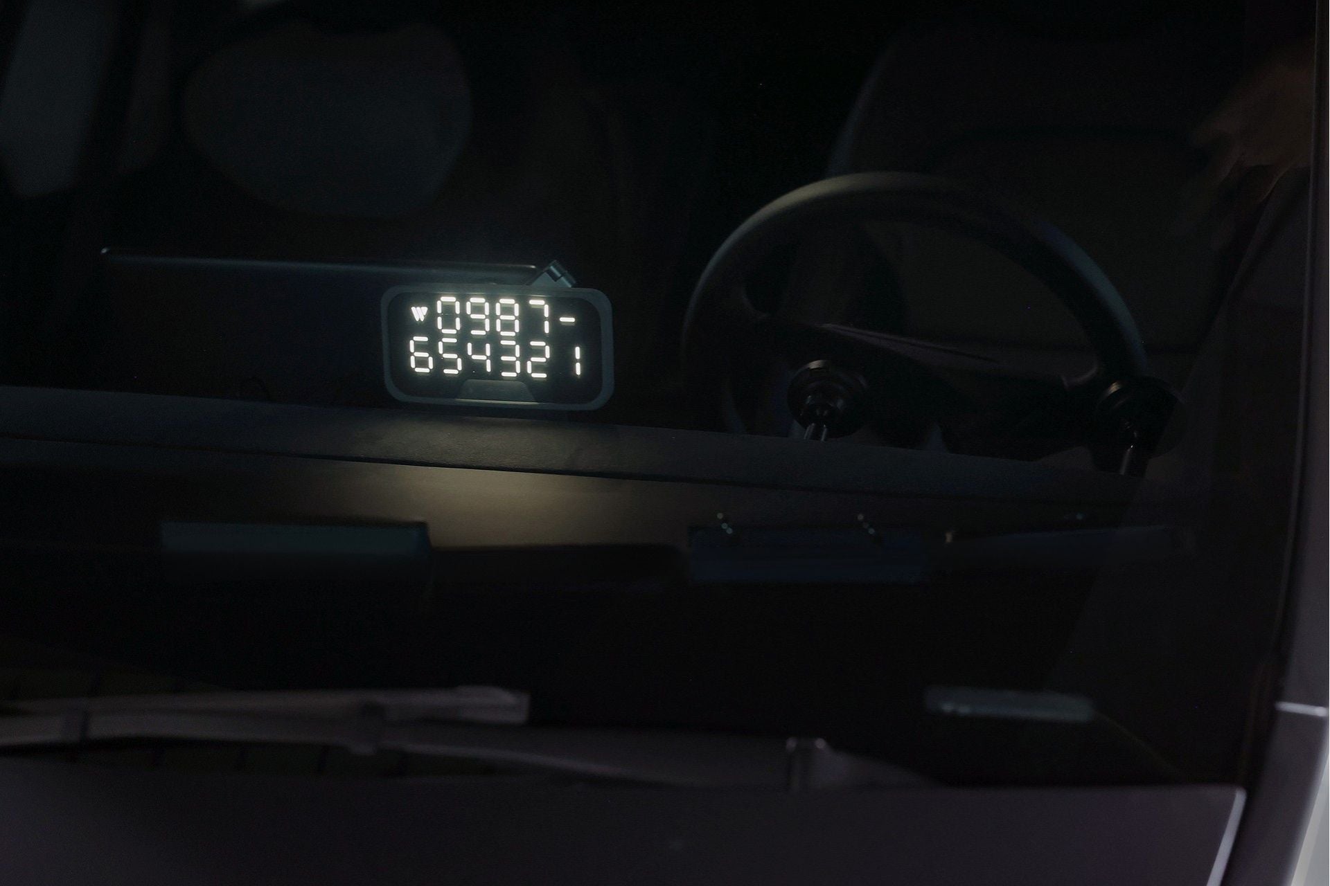 A digital display with numbers “0987 654321” from the JOWUA MagSafe LED Light with Light Stencil Set is visible through a car windshield, positioned on the dashboard near the steering wheel. Next to it, a Tesla wireless charging pad ensures your devices stay powered up effortlessly as you drive.