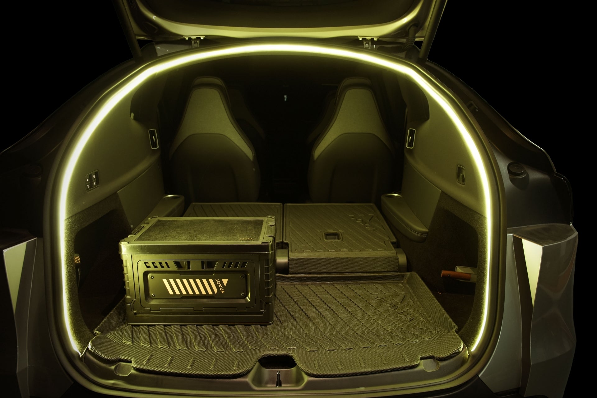 The open trunk of a Tesla Model Y L (2026+) with rear seats folded down, illuminated by yellow ambient lighting, showcases the JOWUA Trunk Storage Bins + Ambient Light Bundle neatly arranged on the cargo mat inside.