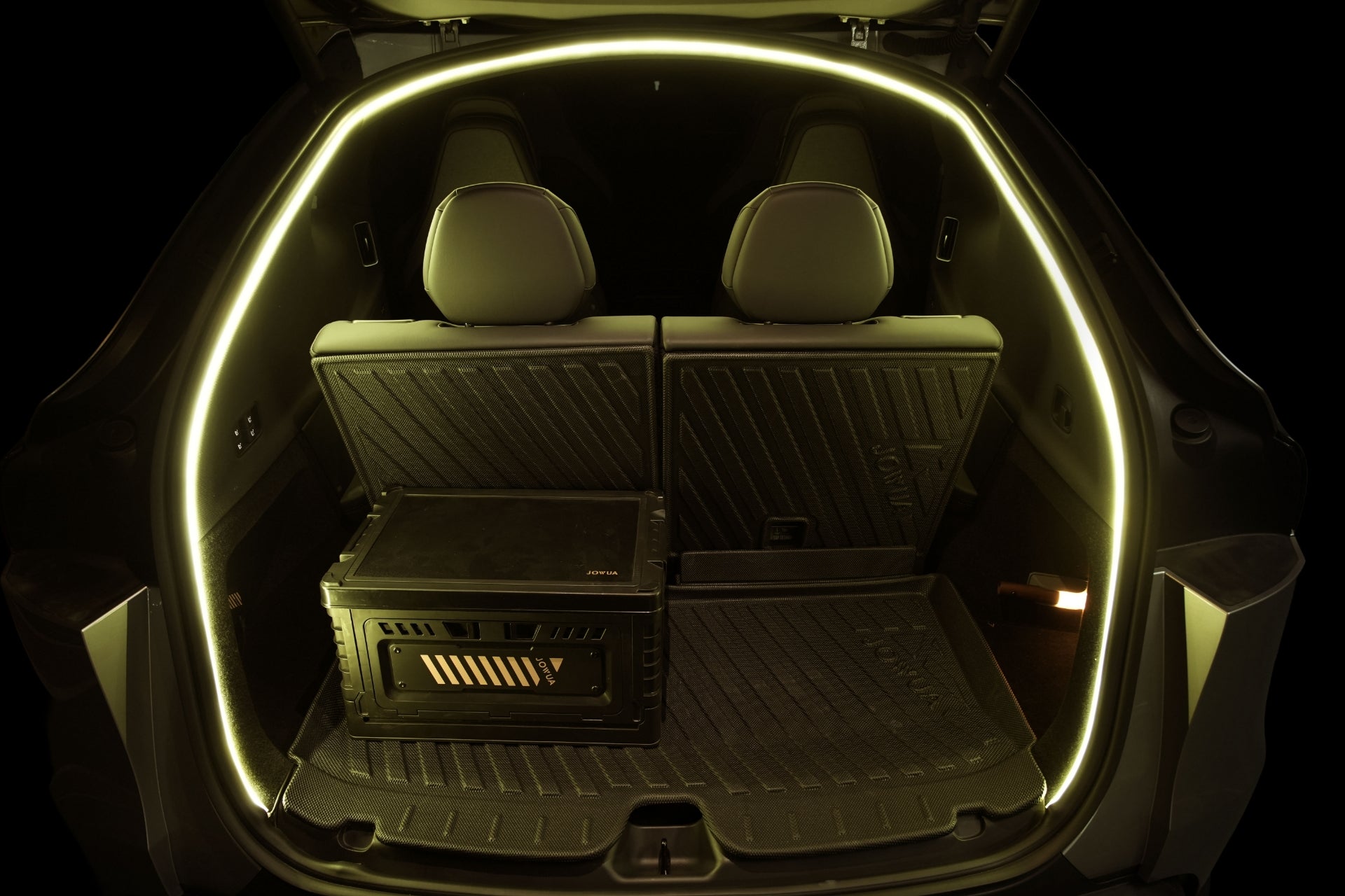 With both rear seats upright, the trunk of the JOWUA Tesla Model Y L (2026+) is illuminated by a yellow ambient LED light strip around the edge. A black JOWUA Trunk Storage Bin from the Storage Bins + Ambient Light Bundle is positioned on the left side of the cargo area, which features protective floor mats.