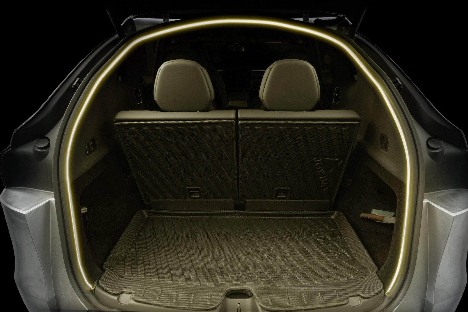 View of an open Tesla Model Y L (2026+) trunk showcasing the cargo area fitted with protective mats, the backs of two rear seats, and a JOWUA Trunk Storage Bin from the Ambient Light Bundle holding a small item on the right side of the trunk floor.