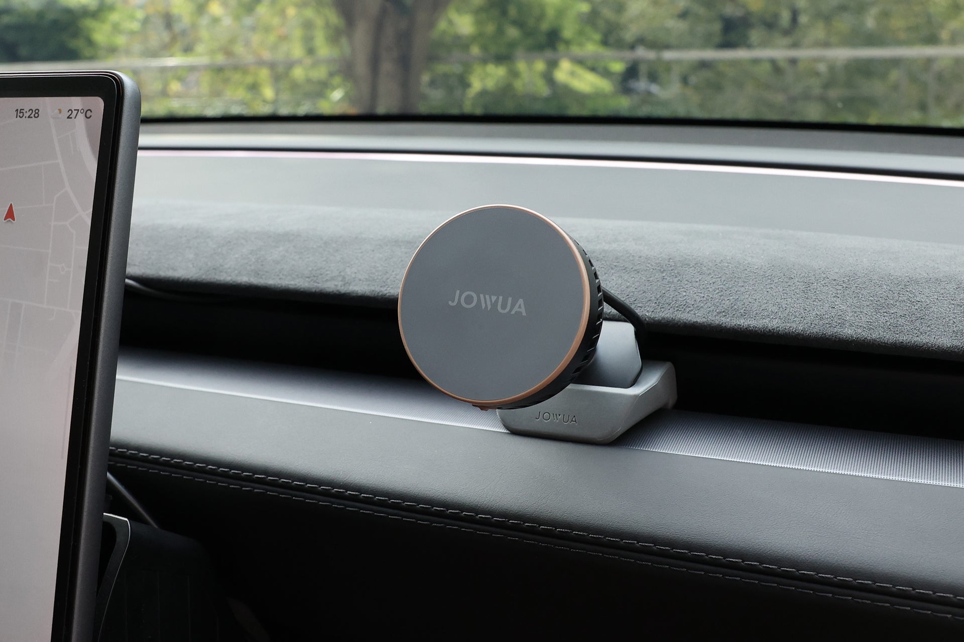A JOWUA Active Cooling MagSafe Car Mount for Air Vents is installed on the dashboard of a Tesla Model 3 Highland, with part of the touchscreen display on the left and trees visible through the windshield in the background.