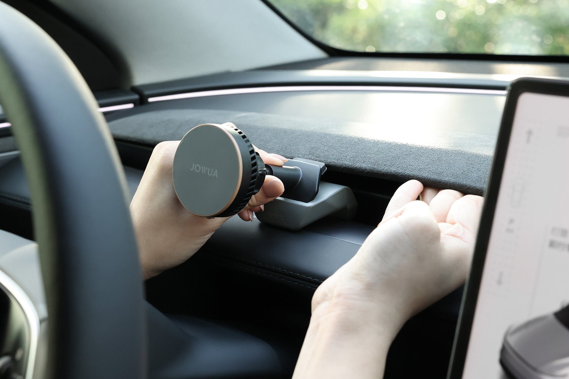A person installs a JOWUA Active Cooling MagSafe Car Mount for Air Vents (Model 3 Highland & Model Y Juniper) on a car dashboard using both hands; a touchscreen is visible, highlighting effortless MagSafe wireless charging.