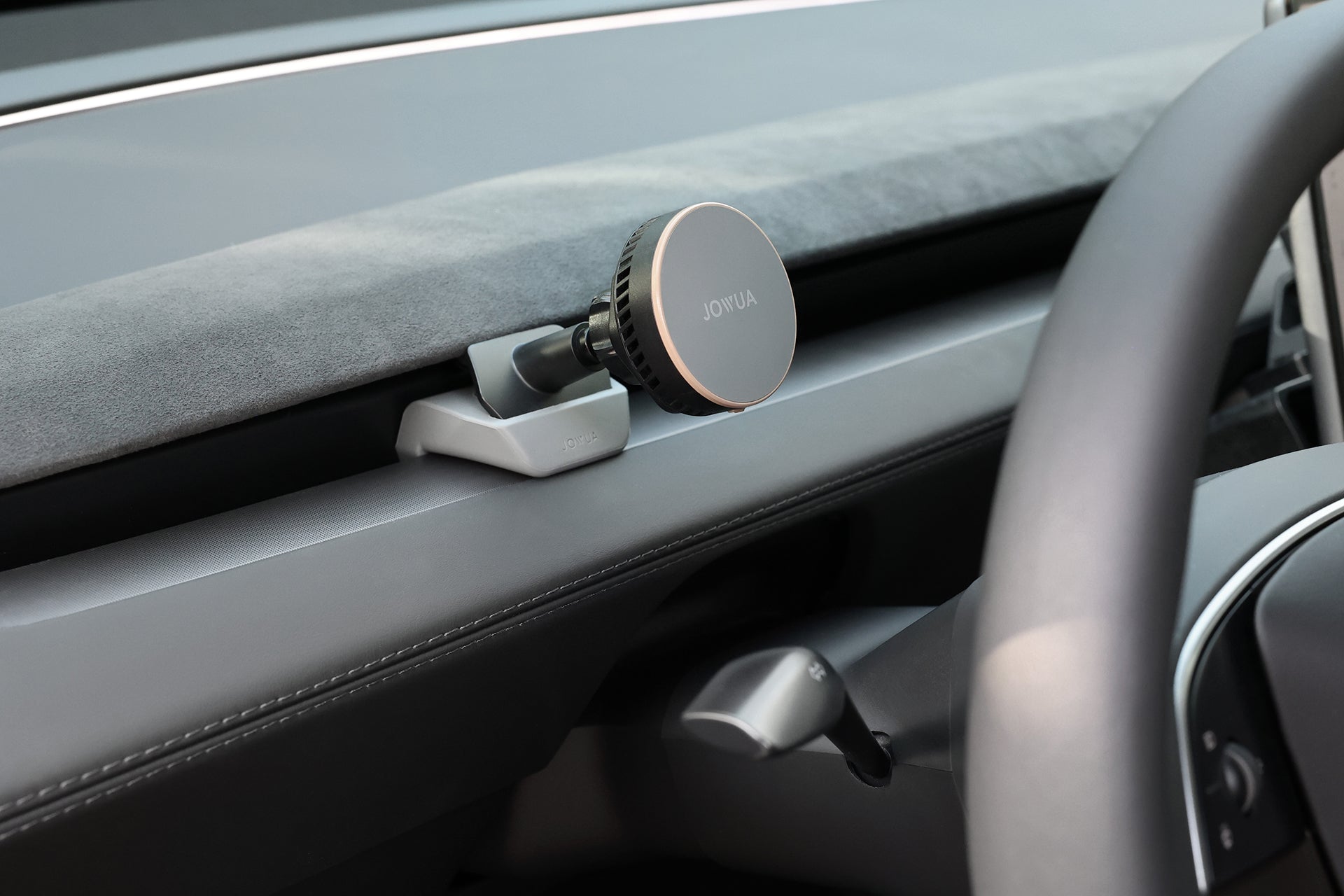 A close-up of a car dashboard shows a JOWUA Active Cooling MagSafe Car Mount for Air Vents (Model 3 Highland & Model Y Juniper) attached above the steering column, featuring a sleek gray base and magnetic Qi2 charging.