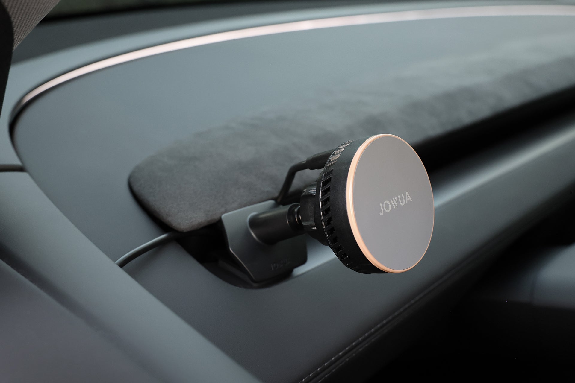 A round, metallic JOWUA Active Cooling MagSafe Car Mount for Air Vents (Model 3 Highland & Model Y Juniper) is attached to a vehicle air vent, with a cable connected for wireless charging.