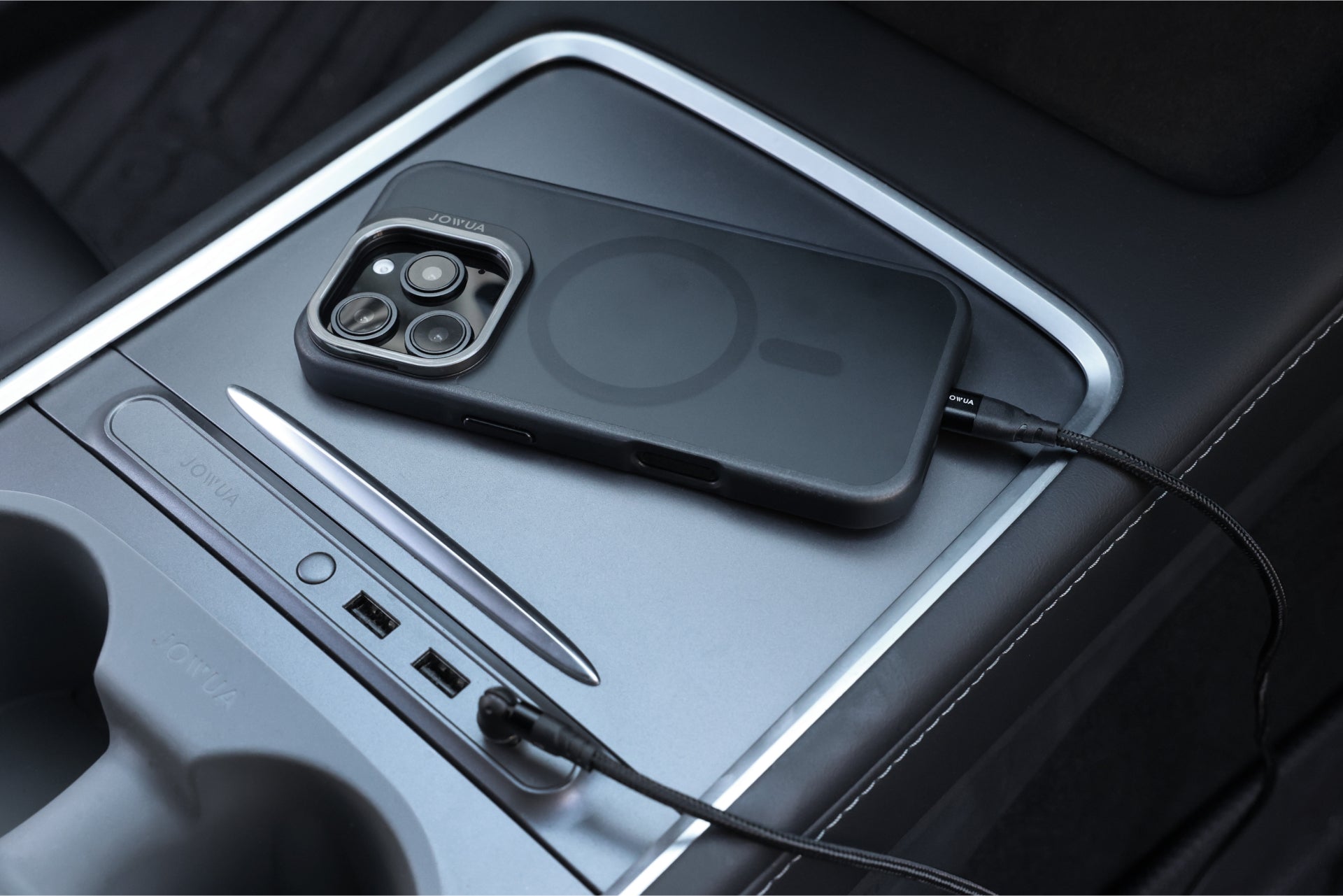 An iPhone 16, protected by a dark JOWUA case designed for Tesla car mounts with MagSafe compatibility and a phone tether tab set, is charging on the car