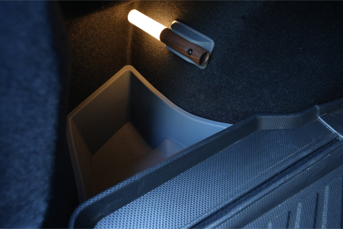 A close-up shows JOWUA Trunk Storage Bins for Tesla Model 3 Highland (2024+), a removable flashlight on the side, a plastic storage compartment on the carpeted floor, and part of a textured rubber floor mat.