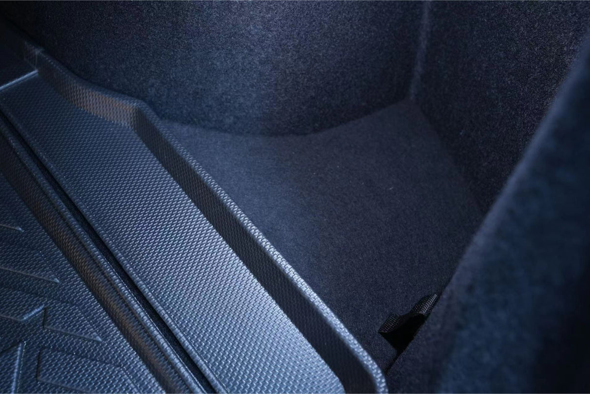 Close-up of a clean, empty Model 3 Highland trunk with dark carpet sides and textured rubber mat. A fabric loop sits on the right—perfect for adding JOWUA Trunk Storage Bins for Tesla Model 3 Highland (2024+).