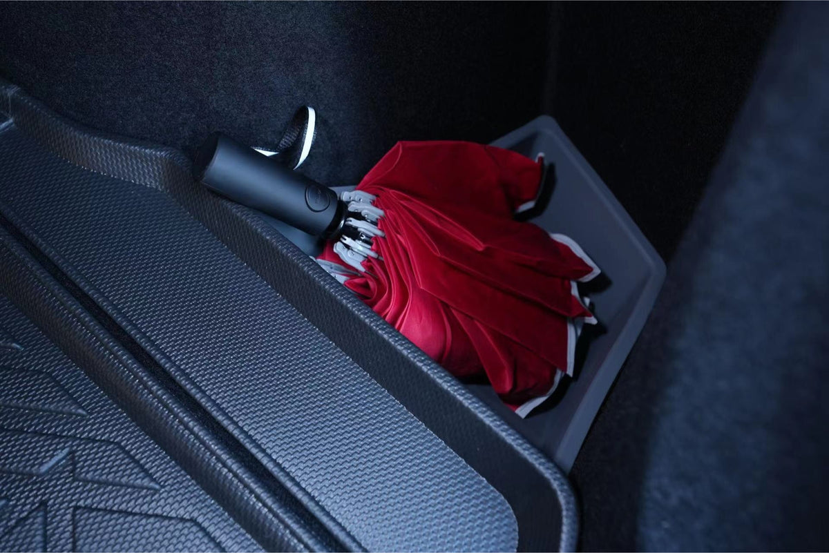 A red folded umbrella with a black handle is stored in a JOWUA Trunk Storage Bin for Tesla Model 3 Highland (2024+), inside the trunk compartment lined with textured black material.