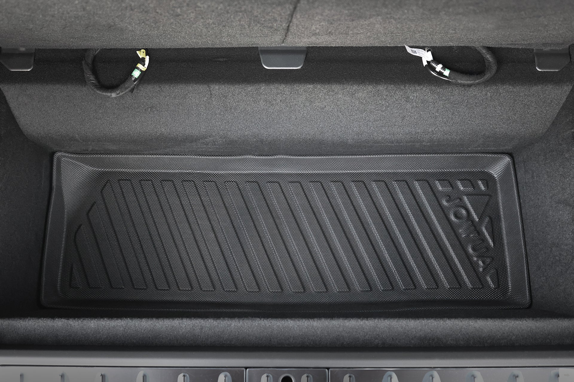 Rectangular black JOWUA All-Weather Shield | Model X Trunk Liner (2021+) with diagonal grooves, placed in the trunk of a car with dark upholstery and two visible cables near the back edge.