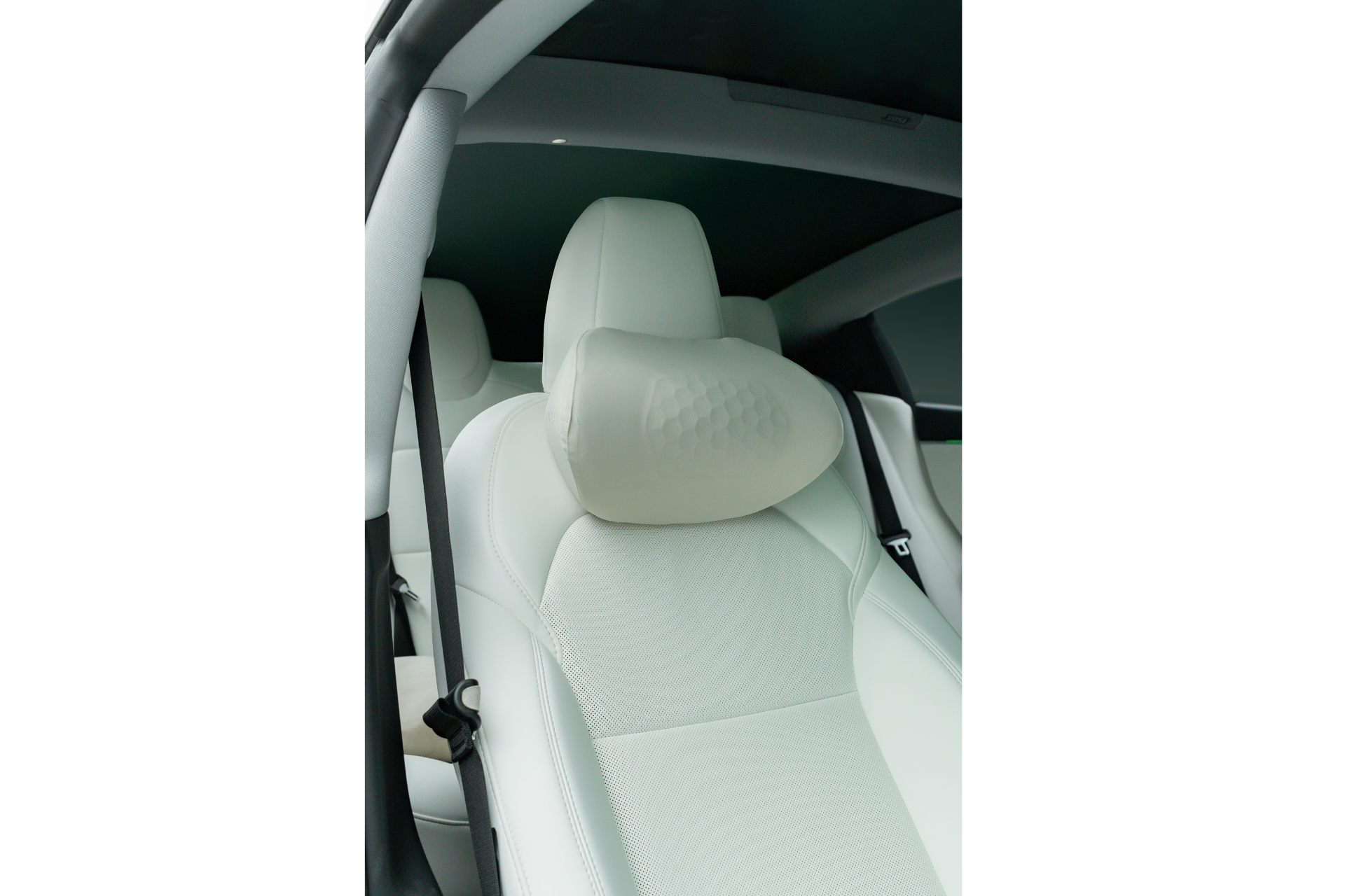 A close-up of a modern car’s front seat in light leather upholstery features the JOWUA Car Neck Pillow with memory foam and a geometric pattern for ergonomic support, along with a seatbelt and part of the door visible.