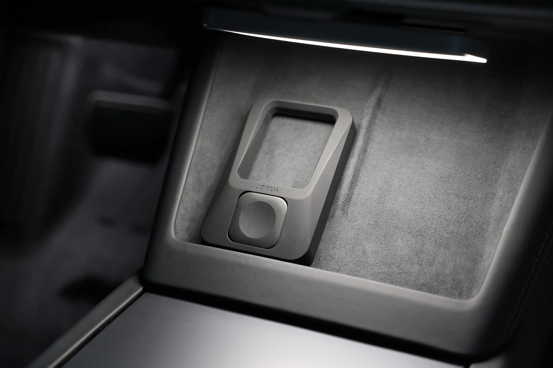 A close-up view of a Tesla center console features the JOWUA Power Dock Combo, an Apple accessory charger with a rectangular design on a velvet-textured surface, softly lit for effortless wireless charging.